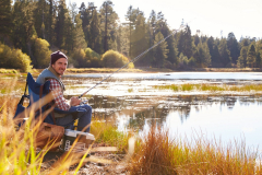 Man fishing by lakeside, looking to camera